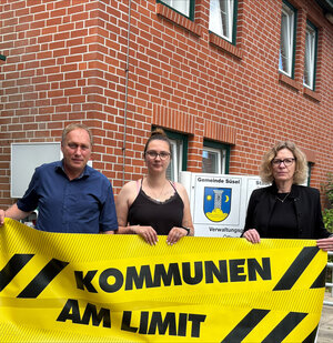 Torsten Bruhn, Lea Beck und Swantje Meininghaus mit Banner vor Rathaus